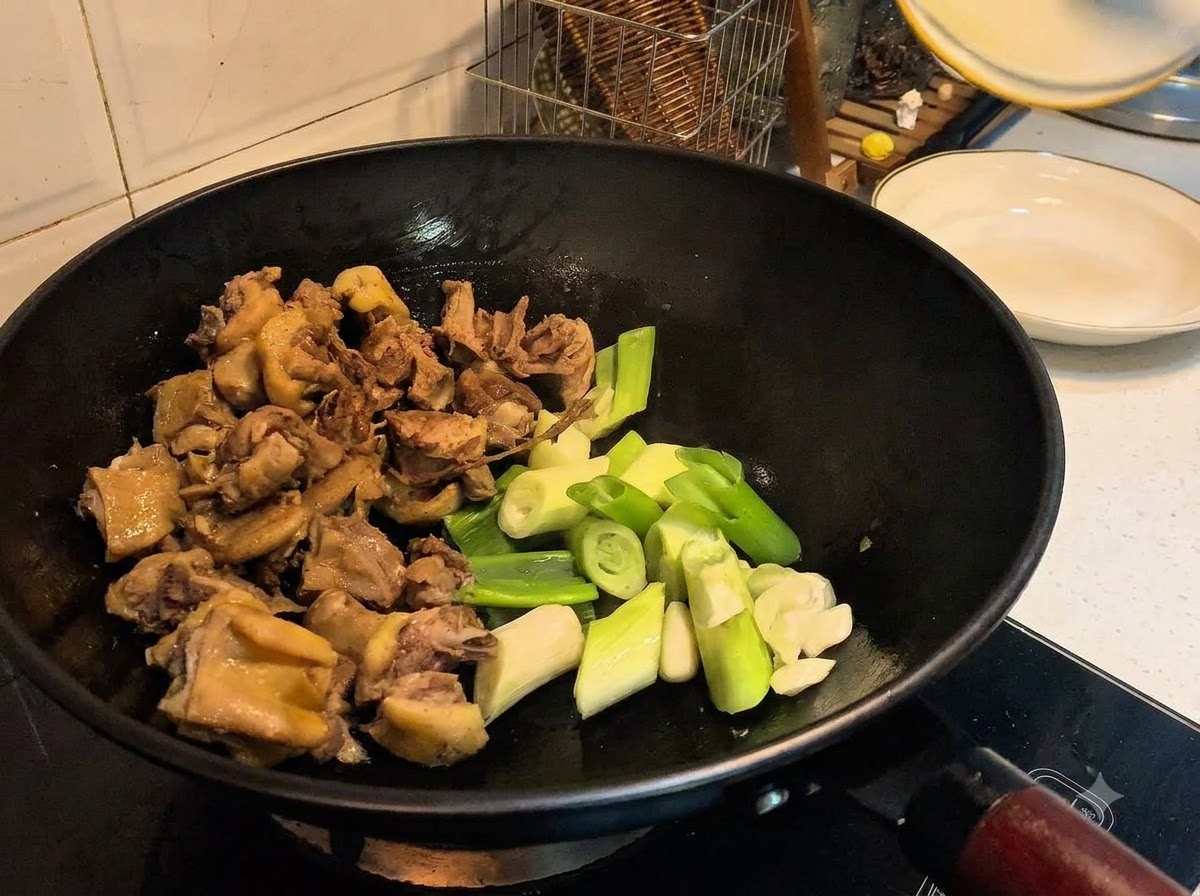 鴨肉と一緒に、刻んだ長ねぎ、にんにく、生姜、スパイスが中華鍋に加えられている様子。