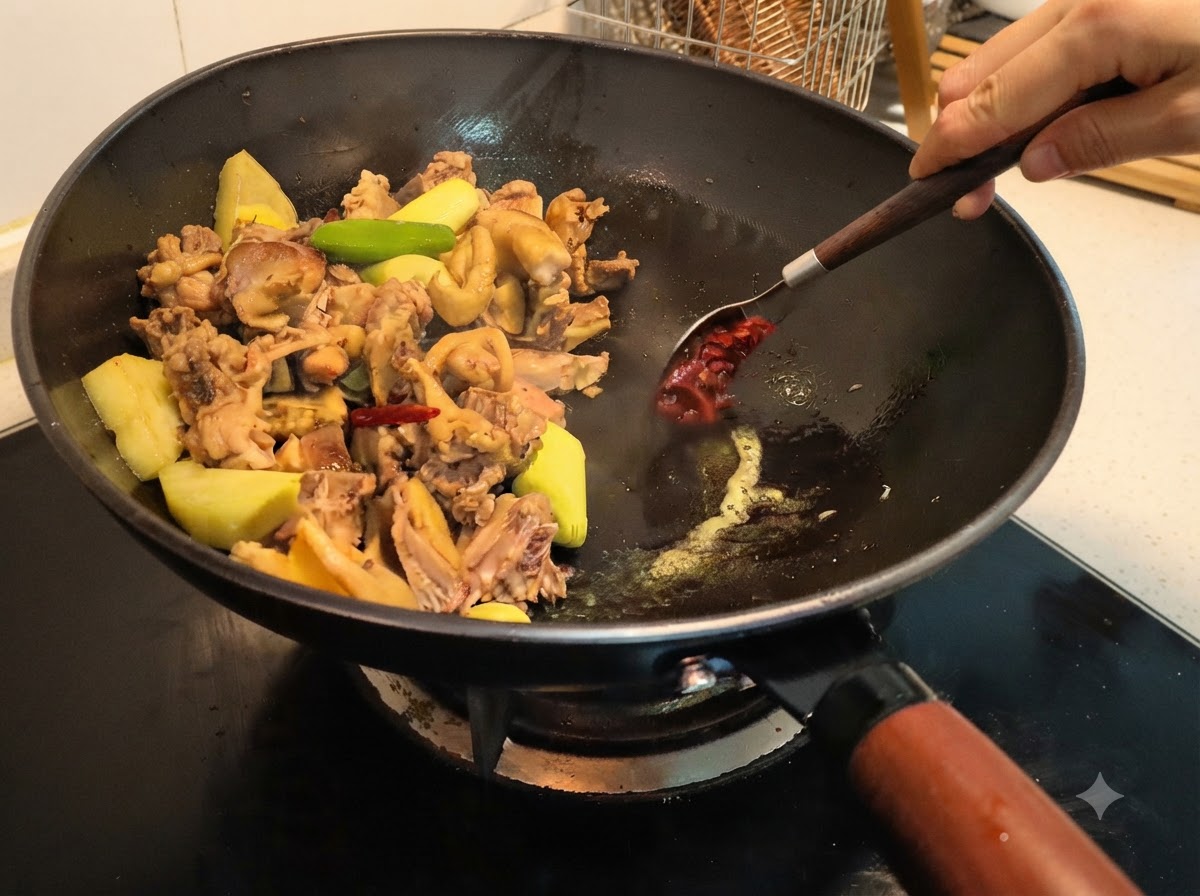 スプーンを使って豆板醤をすくい、中華鍋の食材と混ぜ合わせている様子。