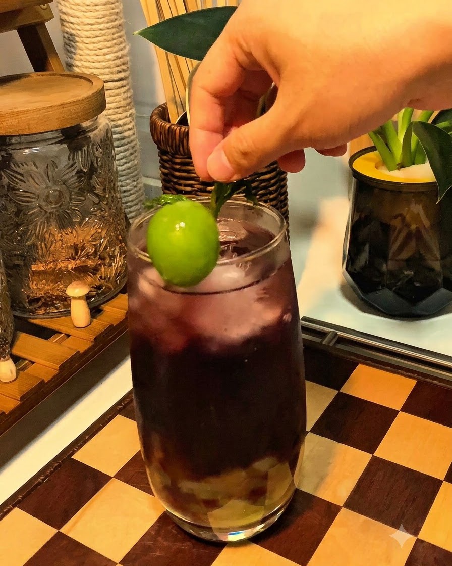紫色のスパークリングドリンクのグラスの縁に、フレッシュな緑ぶどうとミントが飾られている様子。