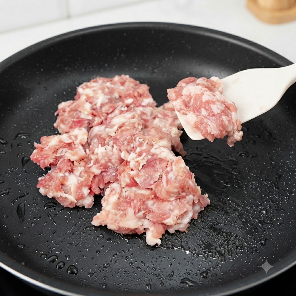 豆腐を焼いた後のフライパンに豚ひき肉を加え、シリコンヘラで炒めている様子