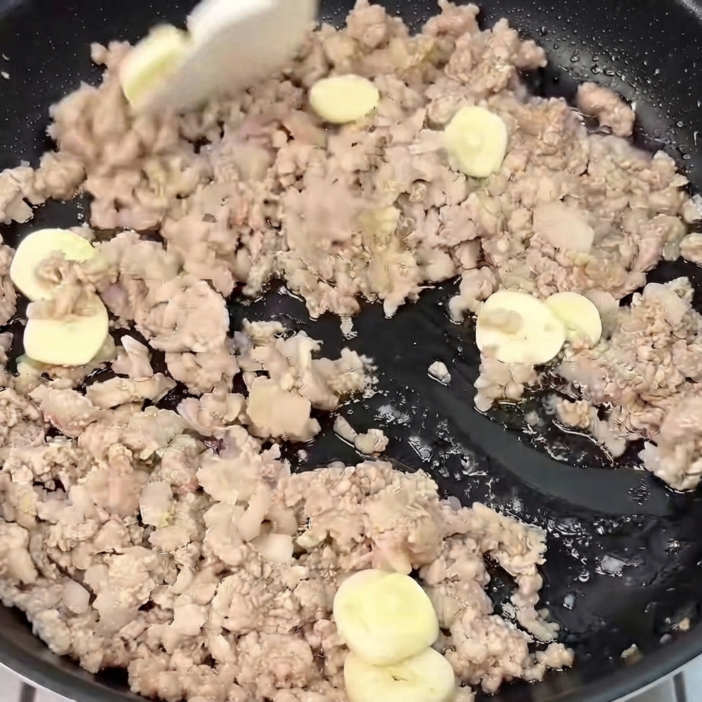 炒めた豚ひき肉に、スライスした生姜とニンニクを加えて一緒に炒めている様子