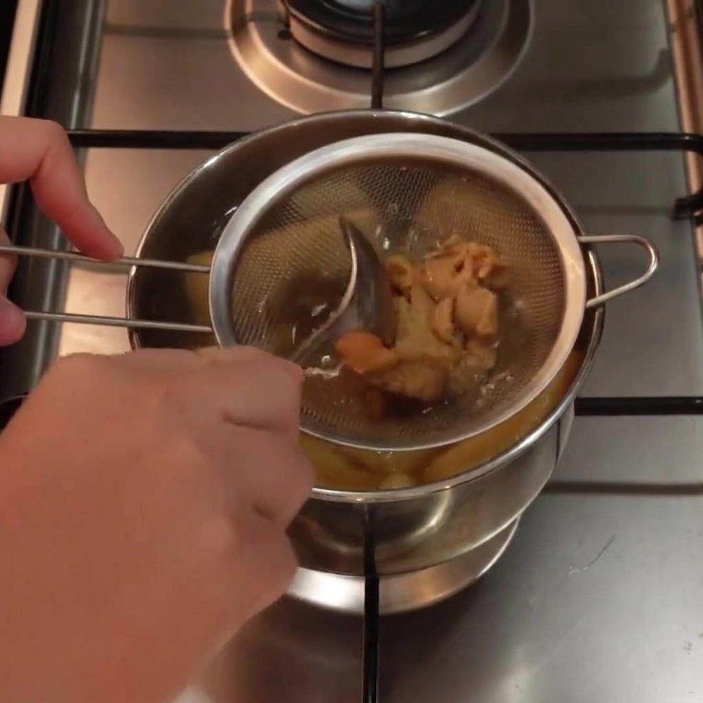 温かいスープの入った鍋の中で、スプーンを使って網じゃくしの中の白味噌を溶いている様子。