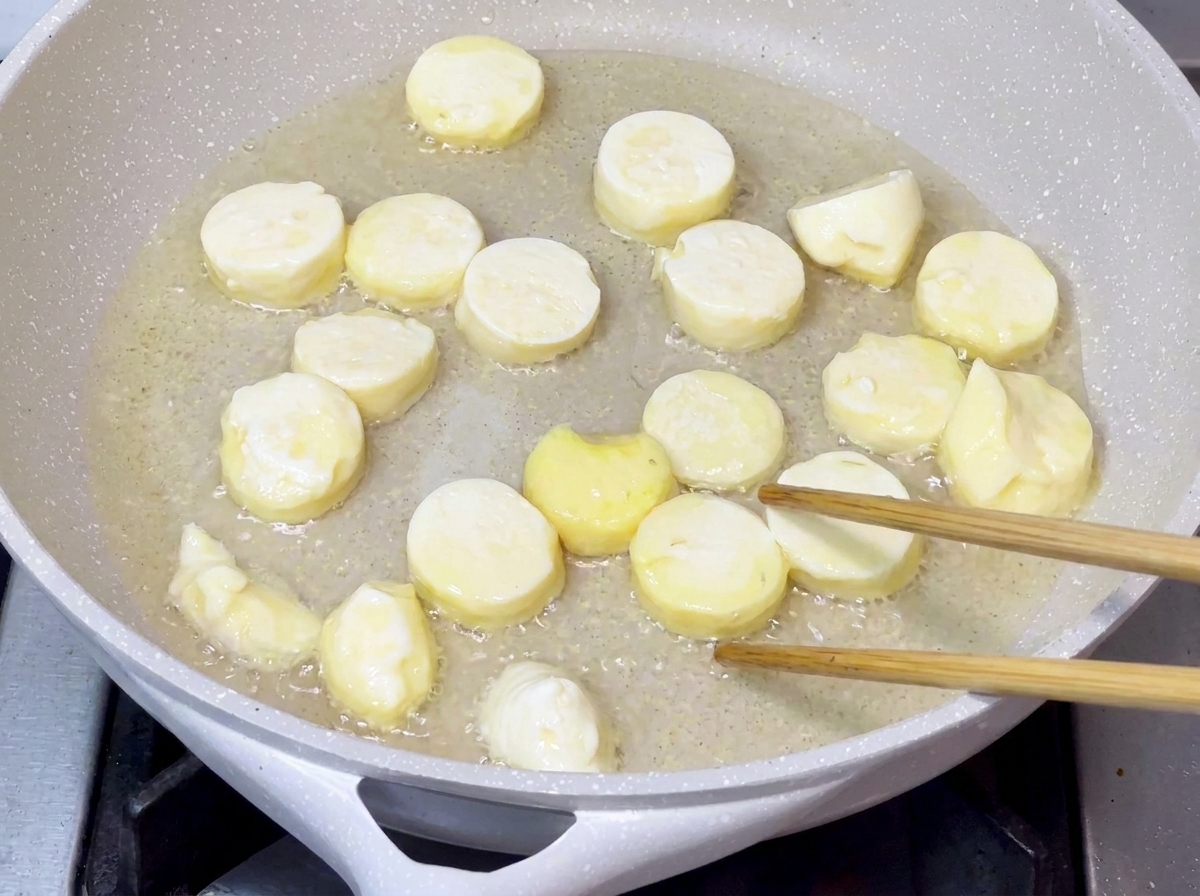 熱した調理油の中で、表面がきつね色でカリッとするまで揚げ焼きにされている豆腐のピース。