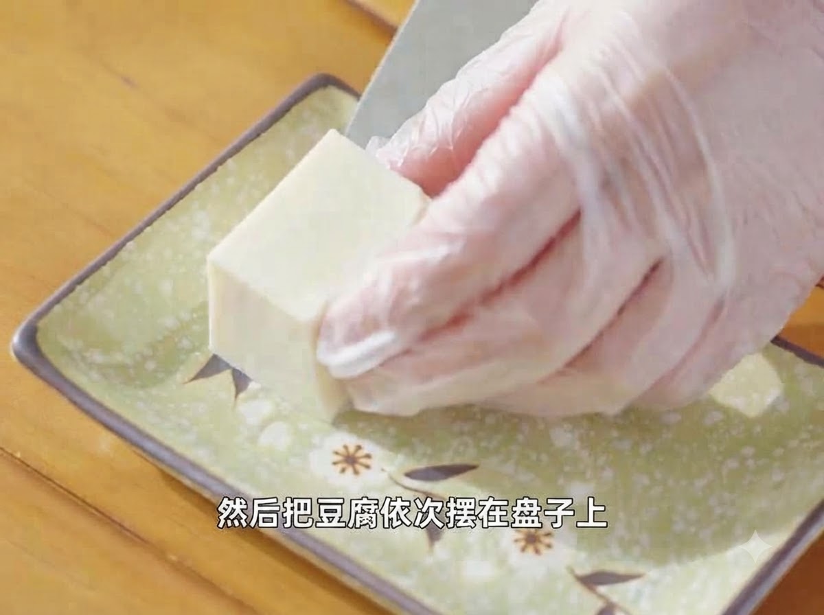 手袋をした両手が、カットした絹ごし豆腐を装飾的な緑色の皿に並べているところ。