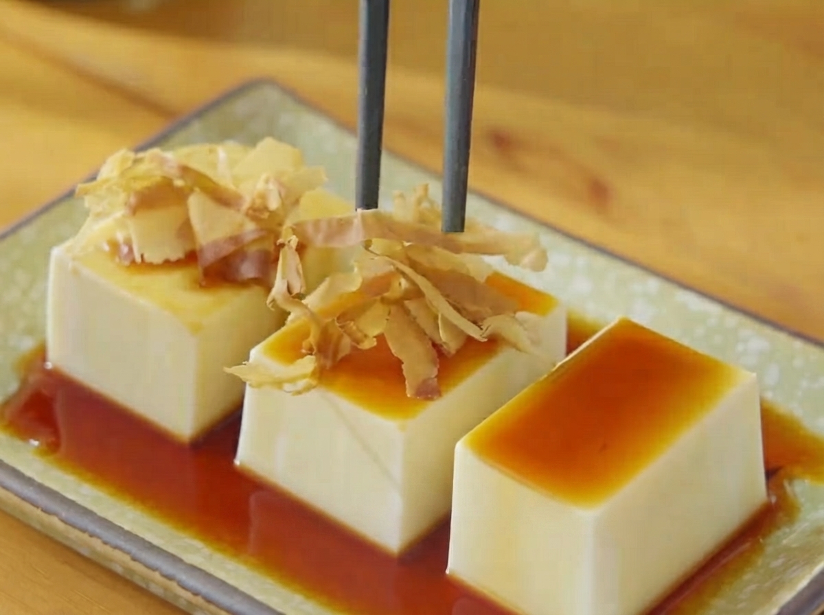 箸を使って、醤油をかけた豆腐の上に乾燥かつお節と海苔をトッピングしている様子。