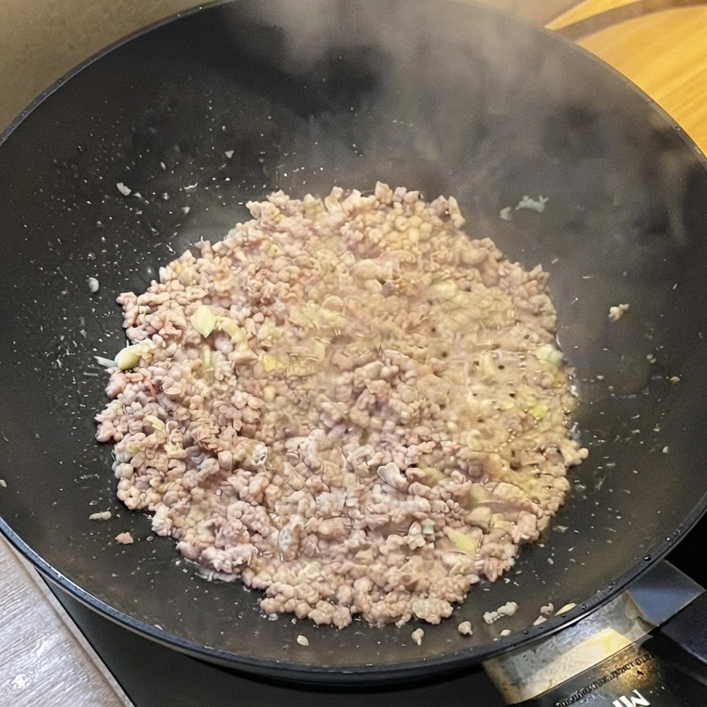 湯気を上げながら炒められたひき肉に、液体調味料が加えられている中華鍋の様子。