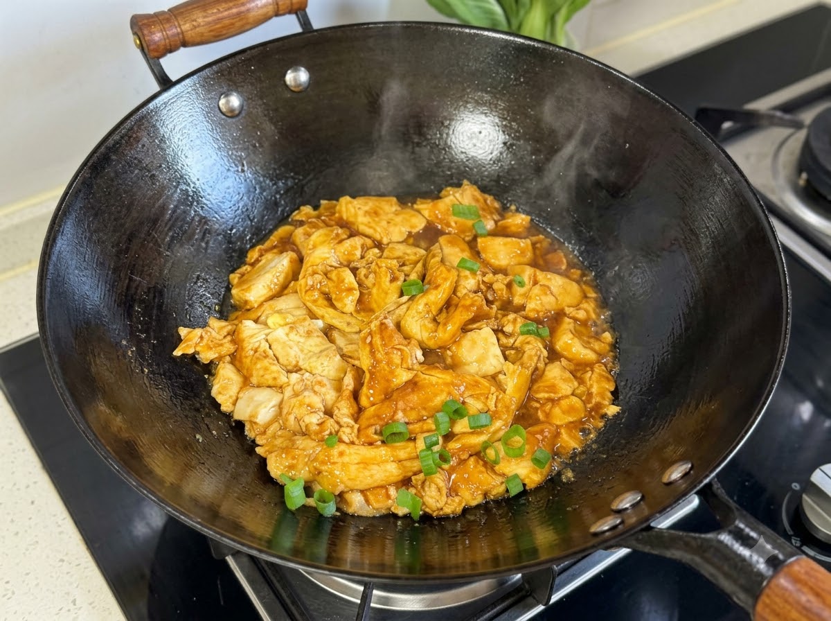 黒い中華鍋の中にある調理された豆腐と卵のミックスの上に、刻んだ細ねぎが散りばめられている様子。