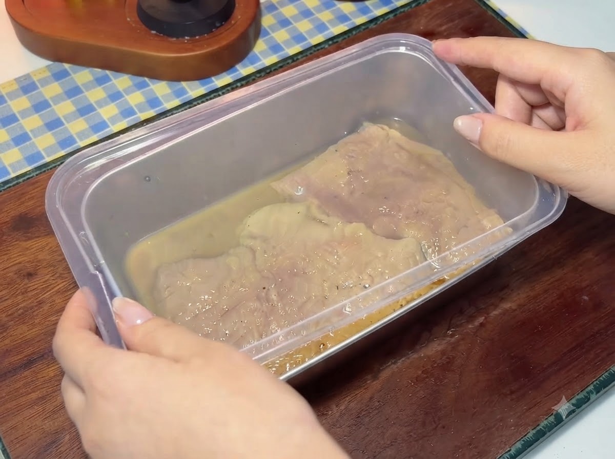 マリネ液に漬け込んだ豚肉が入った容器にプラスチックの蓋を被せている様子。