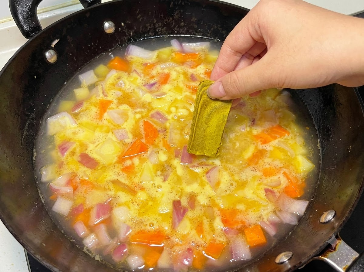 野菜が煮立っている鍋に、固形のカレールーを手で入れている様子。