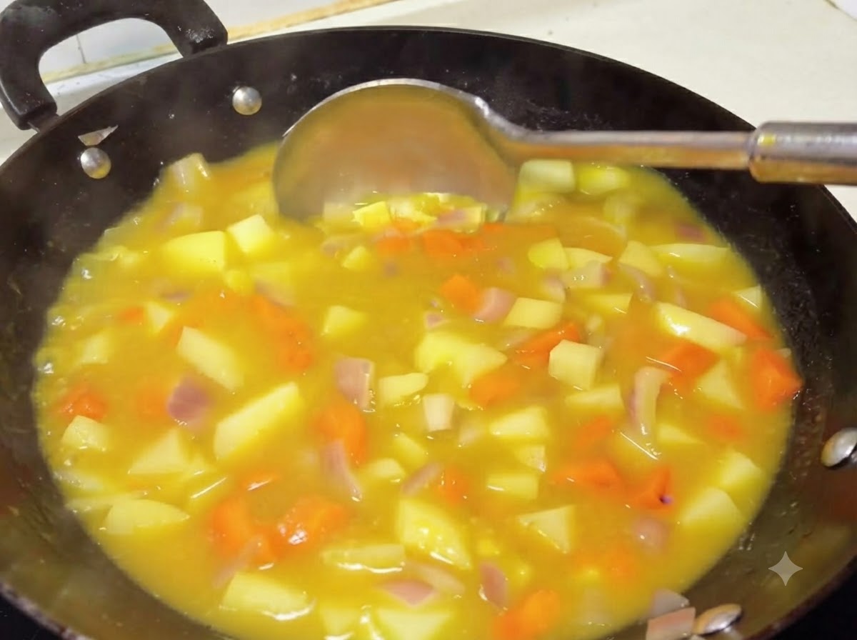 お玉を使って、じゃがいもとにんじんが入った濃厚でとろみのあるカレーソースをかき混ぜている様子。