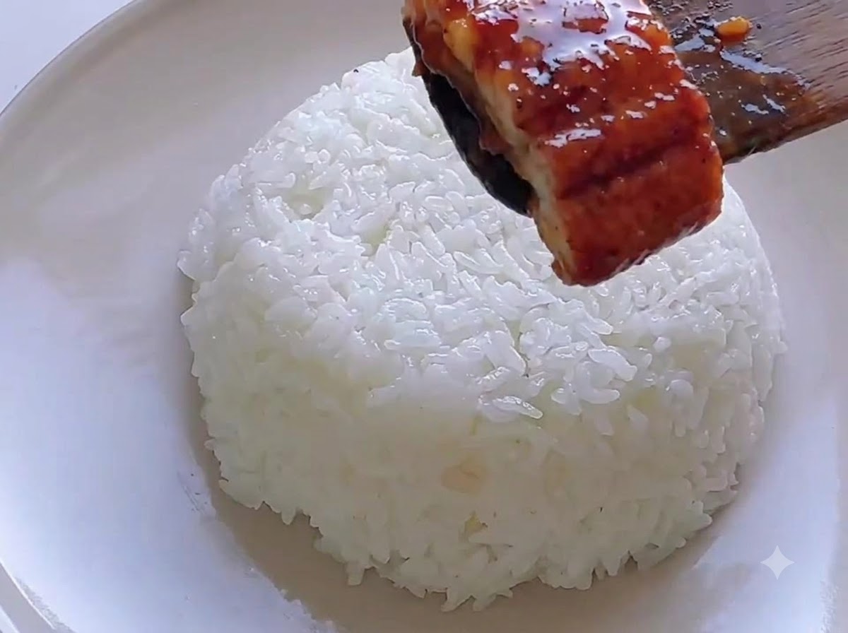 器に盛ったご飯の上に、木べらを使ってうなぎをのせている様子。