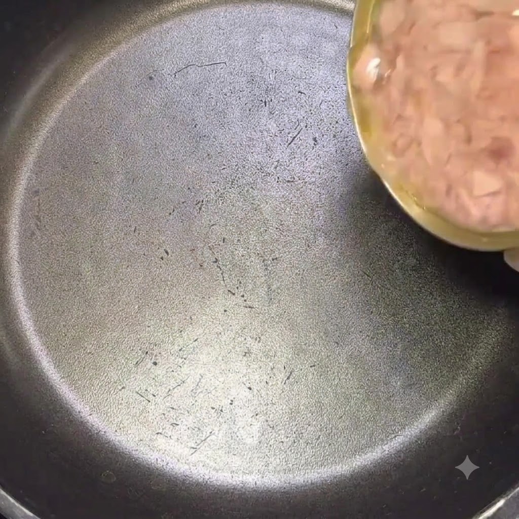 黒いフライパンにツナ缶を油ごと入れている様子。