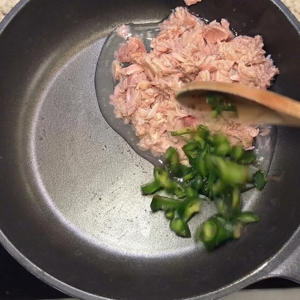 スライスした青唐辛子を、木べらを使ってツナの入ったフライパンに加えている様子。