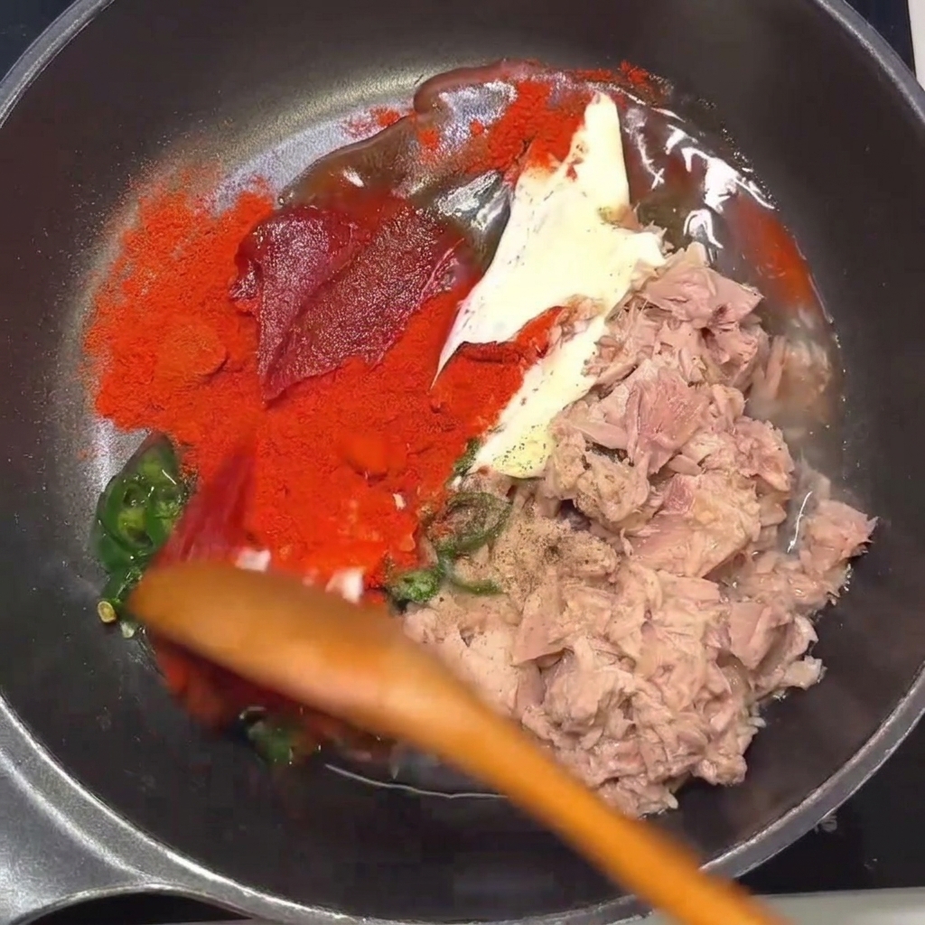 木べらを使って、フライパンの中でツナ、唐辛子、調味料を混ぜ合わせている様子。