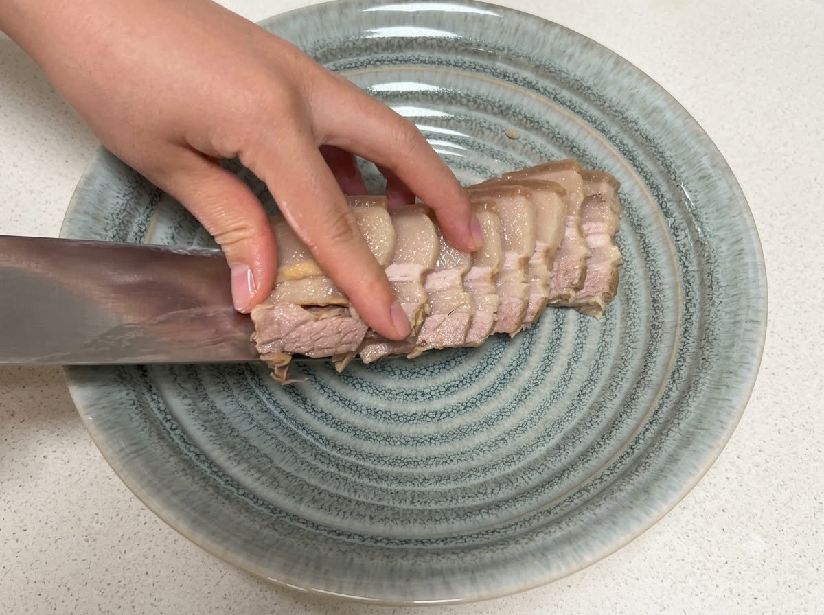 切ったゆで豚を包丁にのせて、グレーの皿に移している様子。