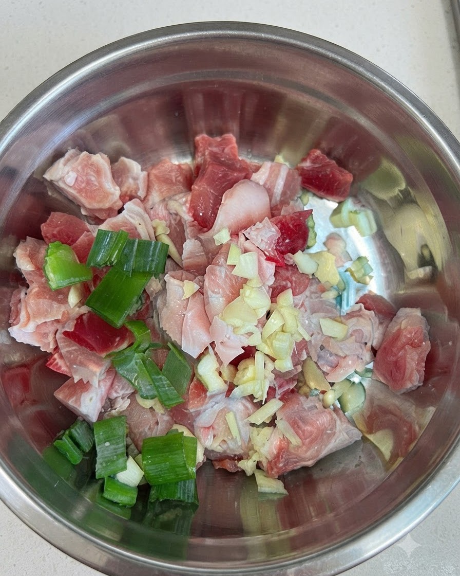 ボウルに入った生のかたまりの豚バラ肉に、にんにく、刻みネギ、赤色のコチュジャンが添えられている様子