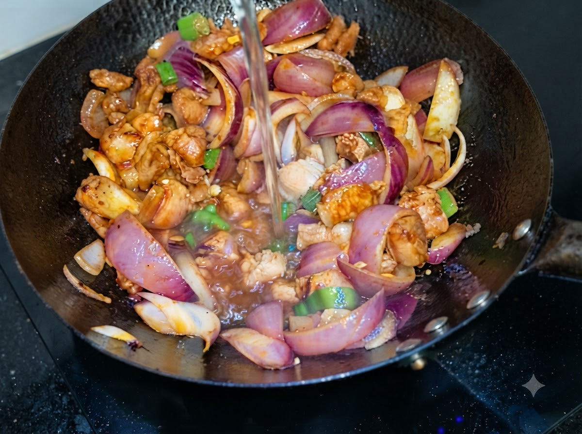 豚バラ肉と紫玉ねぎの炒められた中華鍋の上から、水が注がれている瞬間
