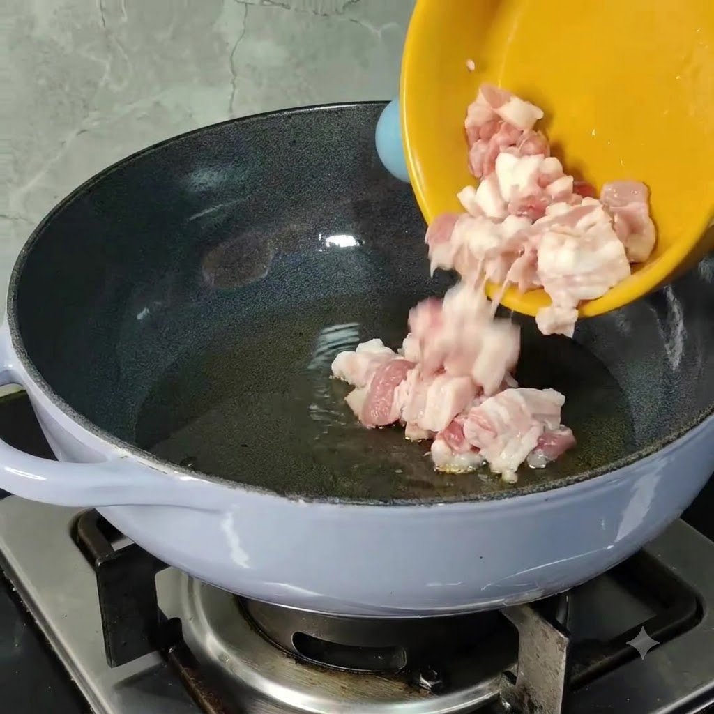 黄色いボウルから、刻んだ生豚バラ肉のピースが油を引いて温めたフライパンに滑り落ちているところ。