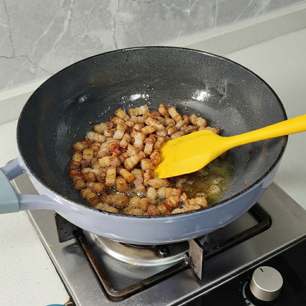 黄色いヘラを使って、フライパンで豚バラ肉のピースが軽くきつね色になるまで炒められているところ。