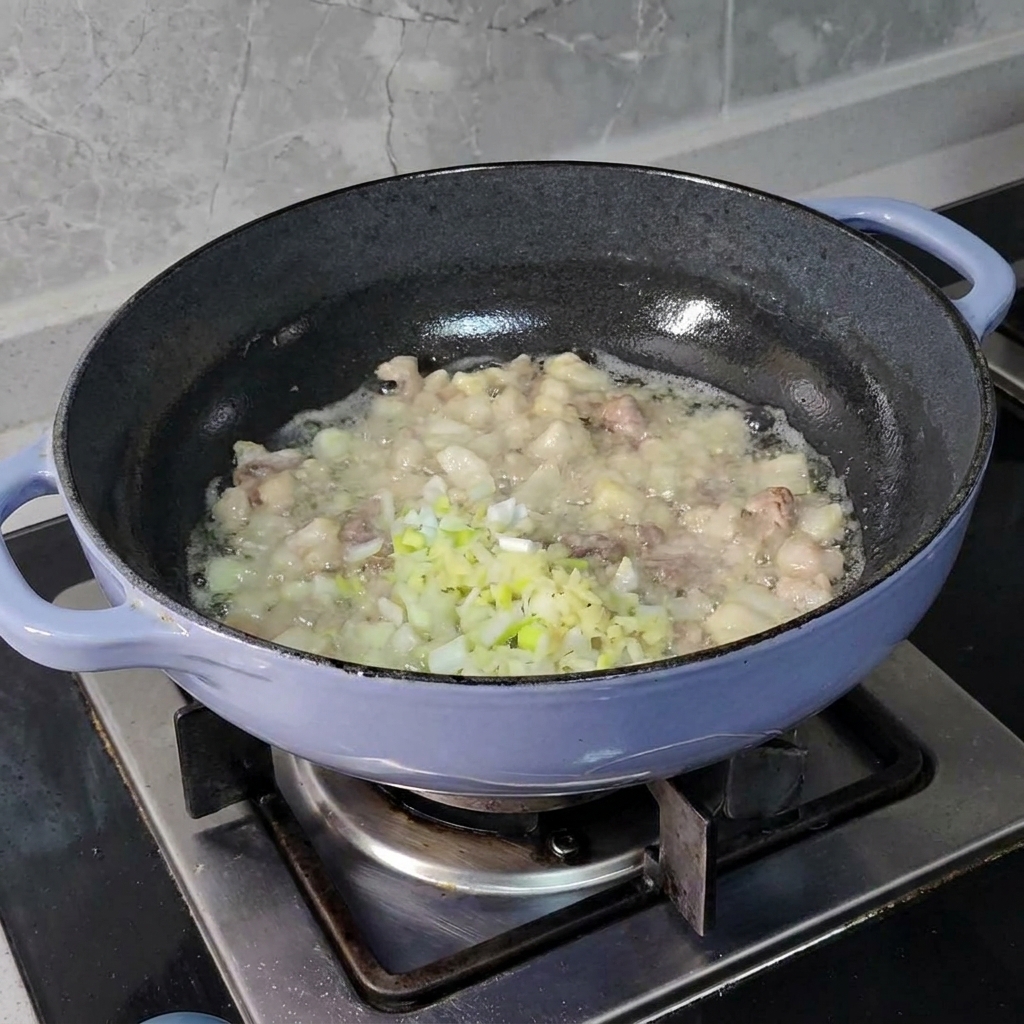 黒いスキレットでジュージューと焼ける豚肉の中に、みじん切りにしたネギ、生姜、ニンニクが加えられているところ。
