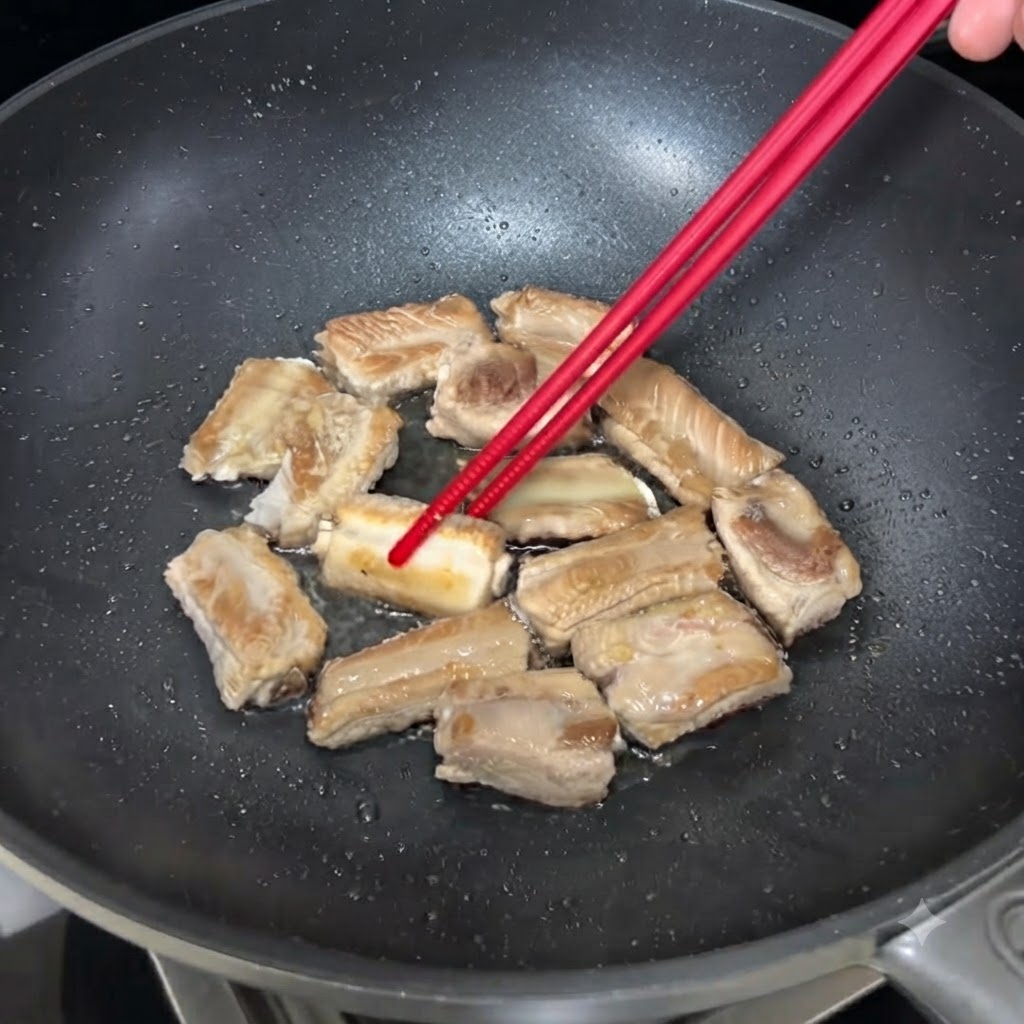 黒いフライパンでジューシーに焼かれ、菜箸で返されている豚スペアリブの様子。