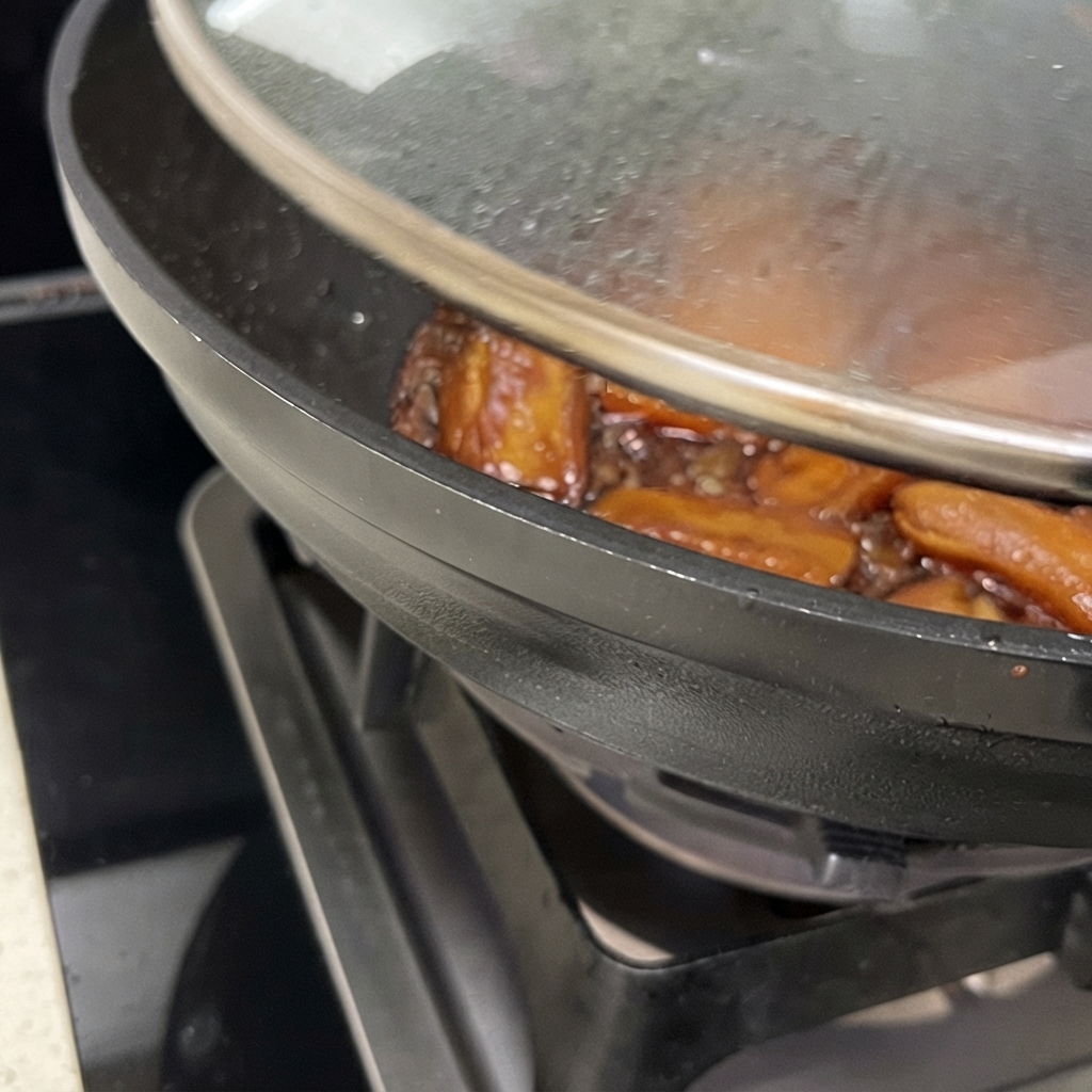 蓋を少しずらした鍋の中で、とろりとした茶色いタレが肉にからみながら煮詰められているアップの写真。