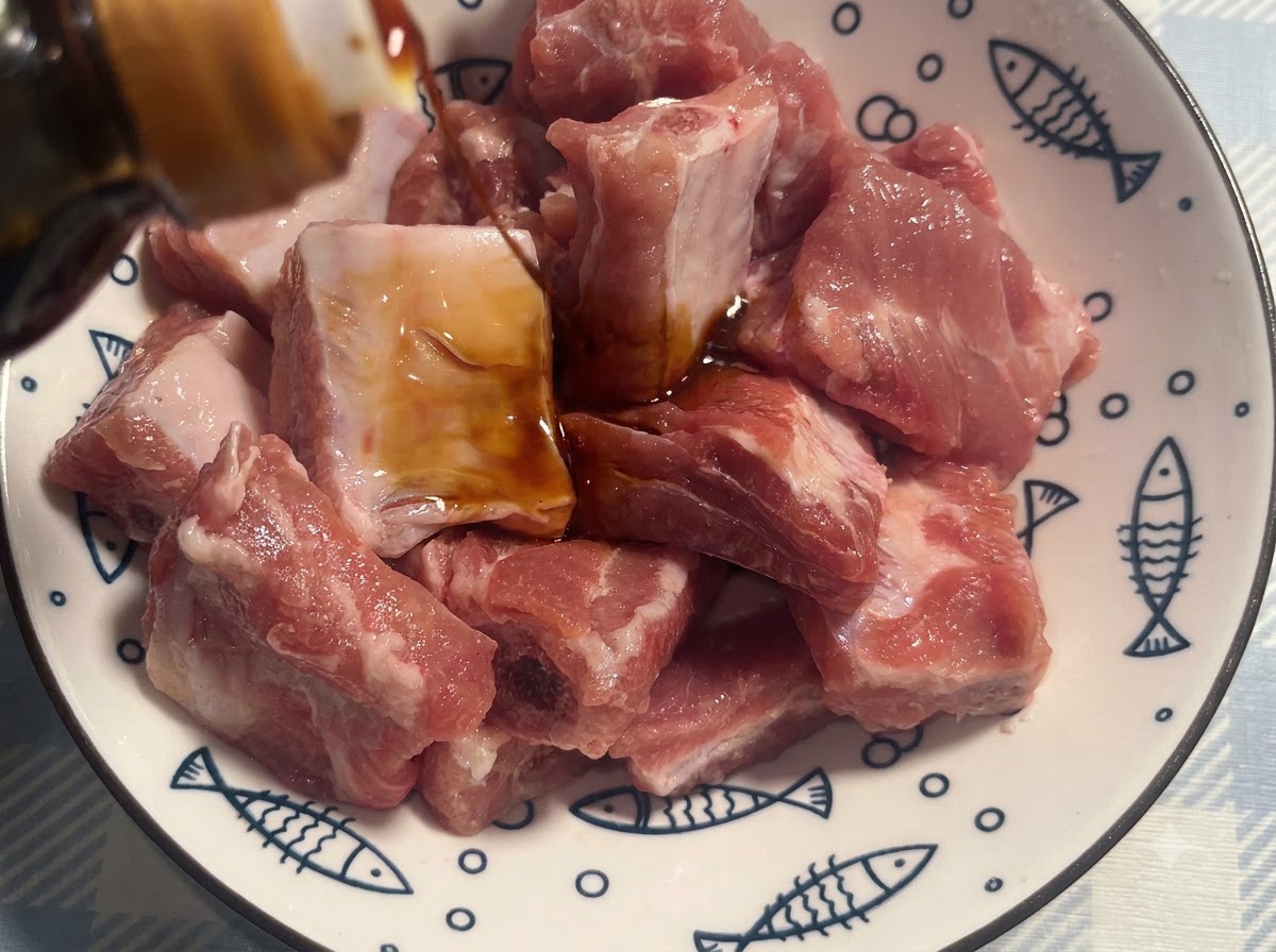白い模様のあるボウルに入ったポークリブに濃口醤油で下味がつけられている様子。