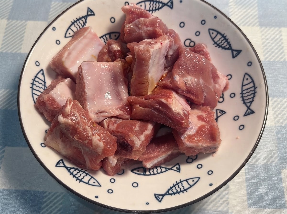 手袋を着用した手が、白い皿の上で味付けされたポークリブを混ぜ合わせている様子。