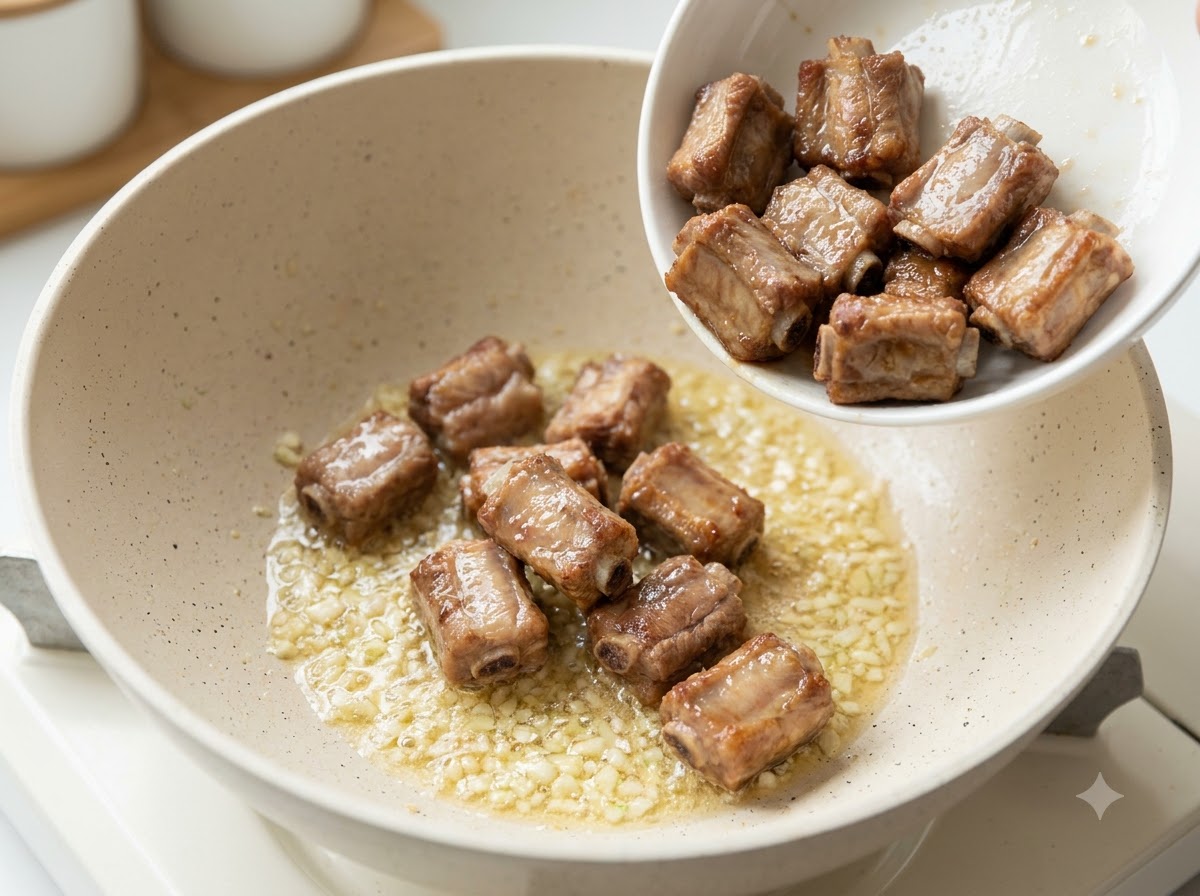 炒めた刻みニンニクとバターが入ったフライパンに、揚げ焼きしたポークリブが投入されている様子。