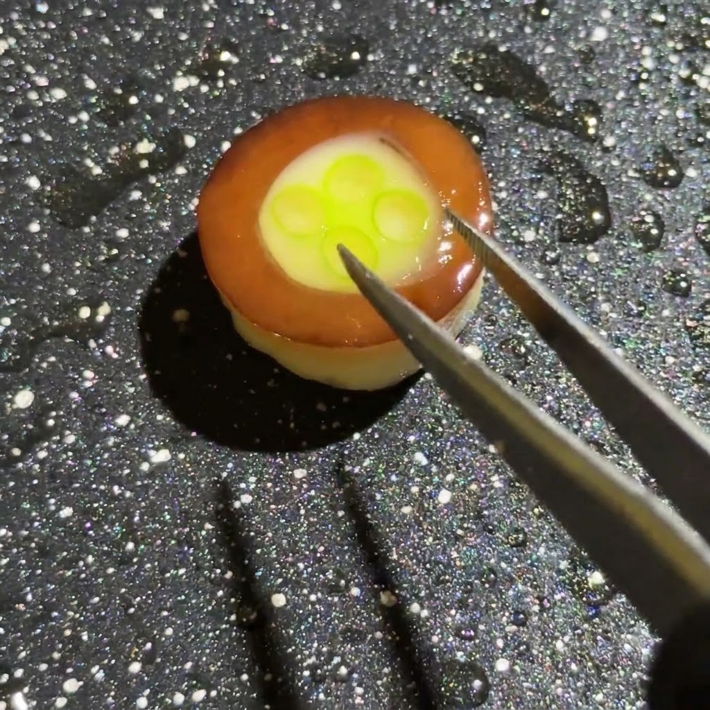 ピンセットとスプーンを使って、キノコリング内の卵と万能ねぎのベースの上に、色鮮やかな刻みハム、玉ねぎ、キノコを追加している様子。