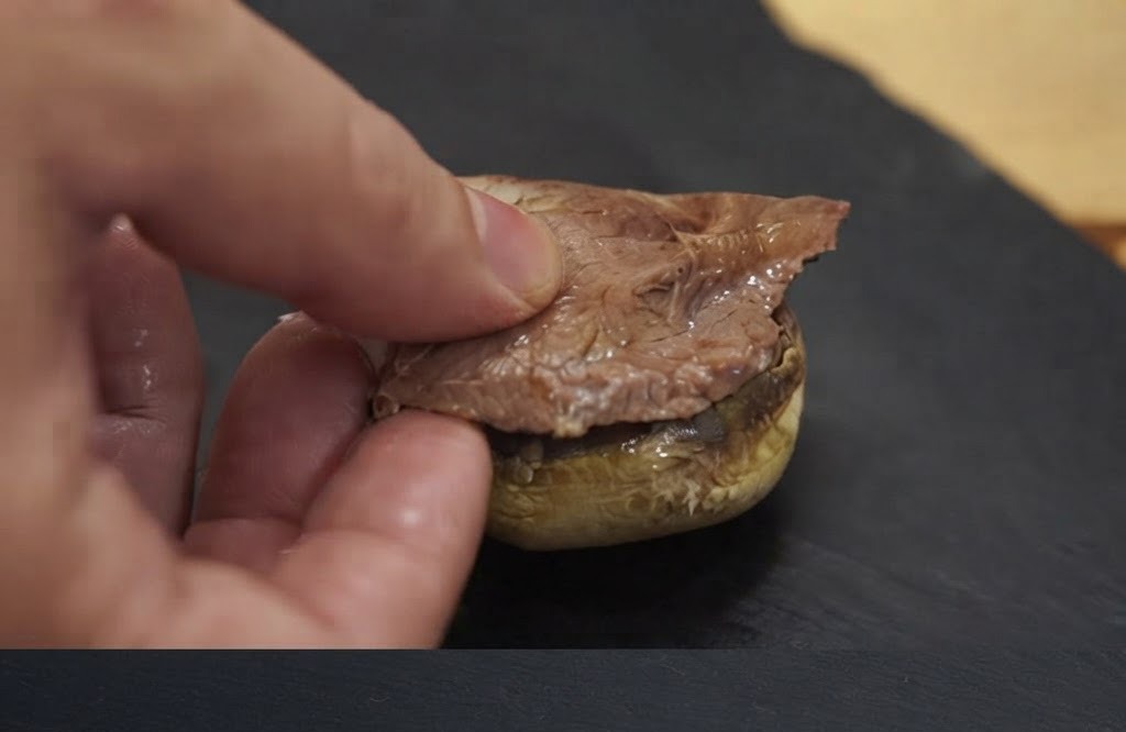 焼き上がったマッシュルームのベースの上に、手でお肉のピースを乗せている様子。