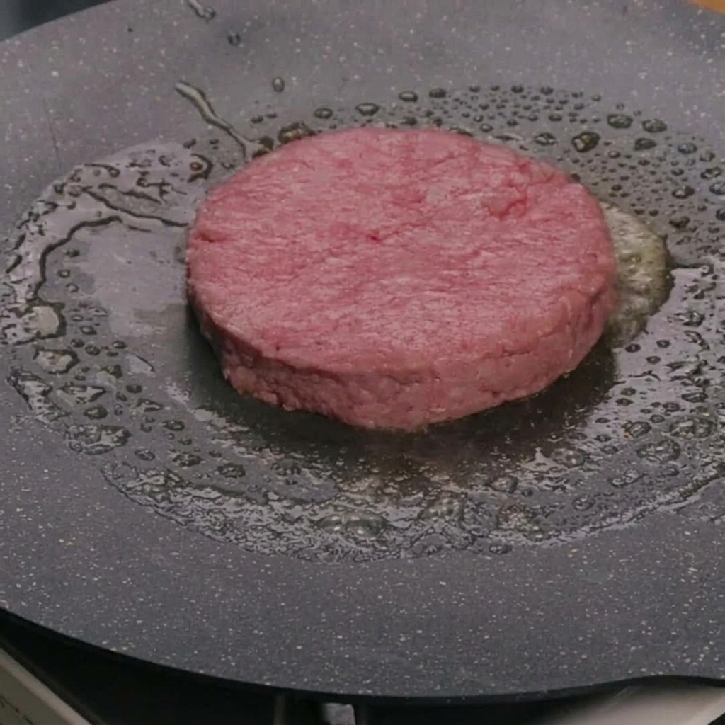 熱したフライパンのバターの中で生ビーフパティを焼いている様子。