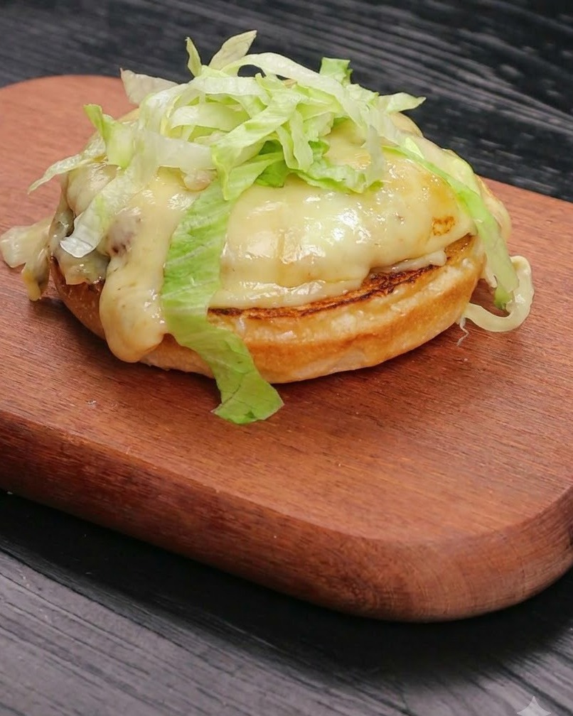 トーストしたバンズの土台に乗った、とろけるチーズとビーフパティの上に、新鮮な千切りレタスがきれいに山盛りになっている様子。