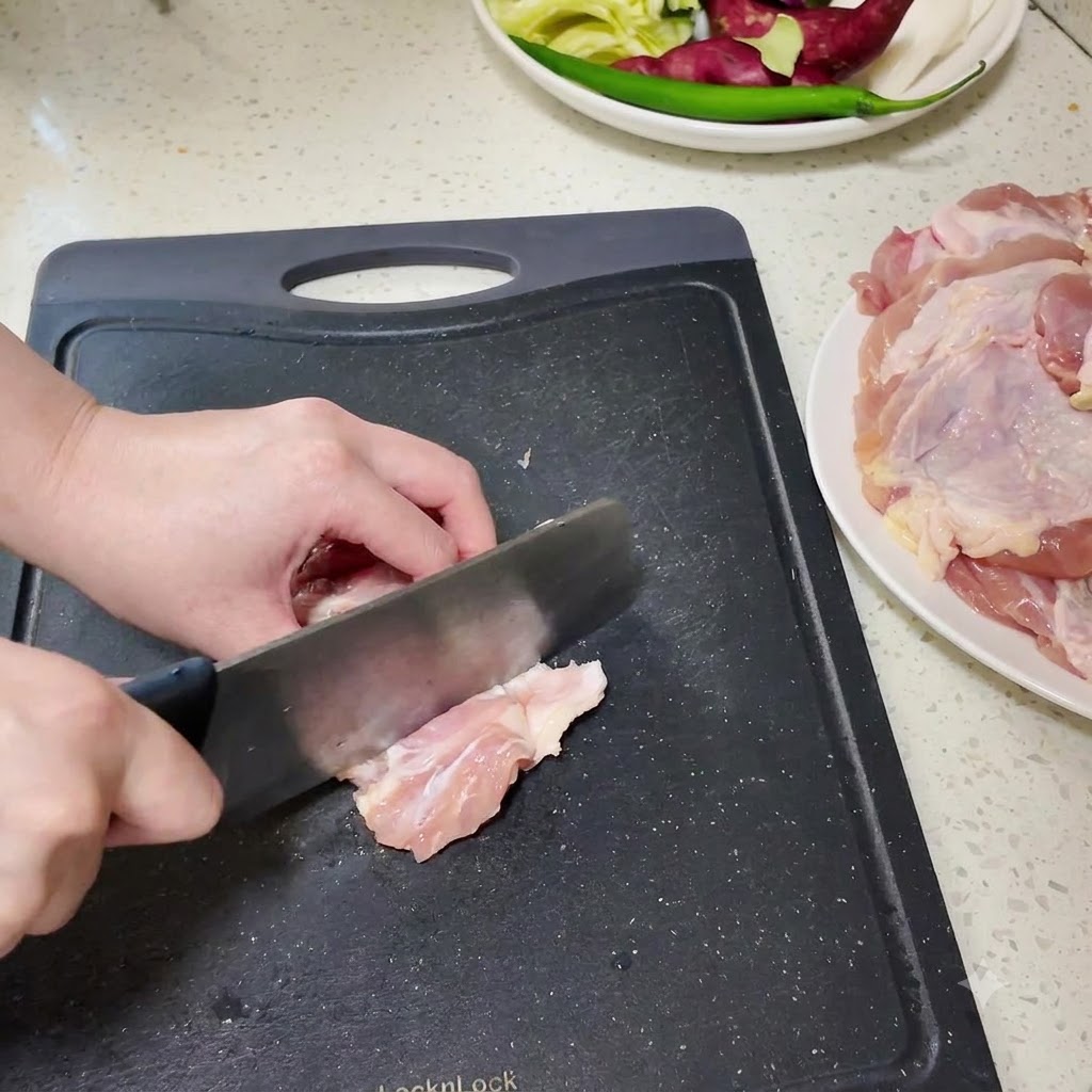 黒いまな板の上で、骨なし鶏もも肉を包丁で小さく切り分けている様子。