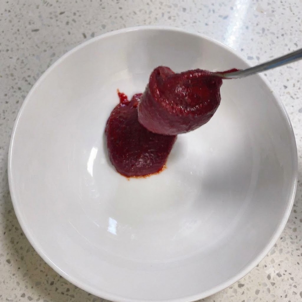 白いボウルの中で、コチュジャンなどの調味料がスプーンで混ぜ合わされている様子。