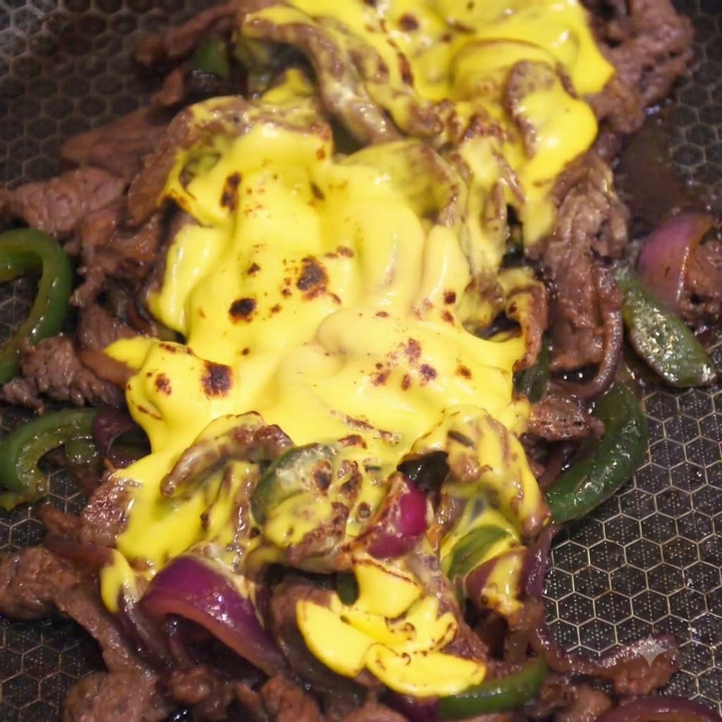 フライパンの中の牛肉ミックスの上の溶けた黄色いチーズのトッピングを、キッチン用の炎で炙っている様子。