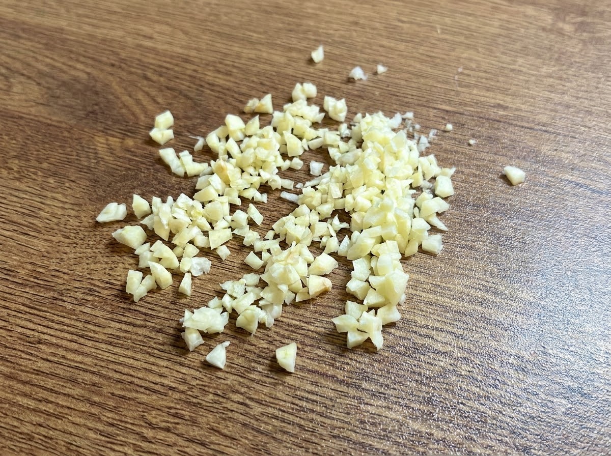 木製のまな板の上に置かれた、細かくみじん切りにした新鮮なニンニクの山。