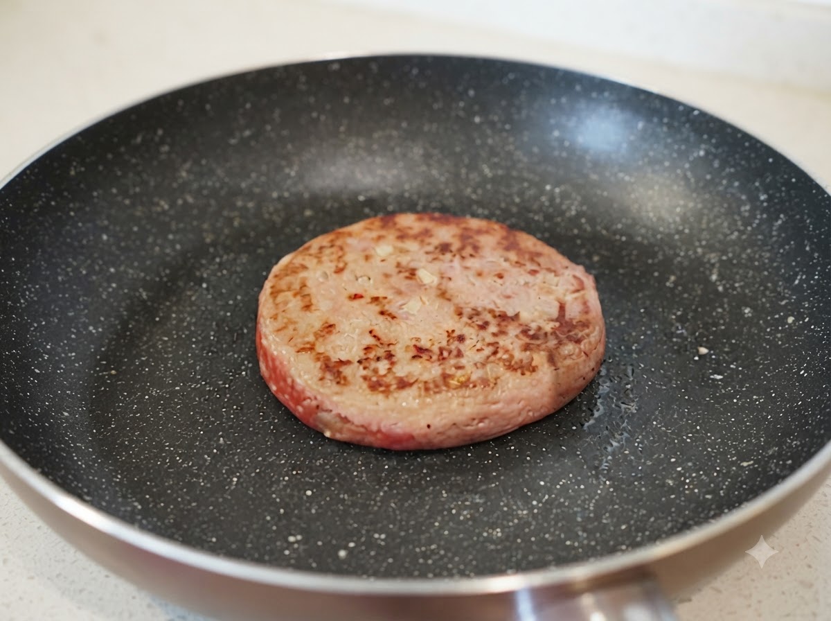 焼き色がついたハンバーグの横で、フライパンに少量の水が注がれている様子。