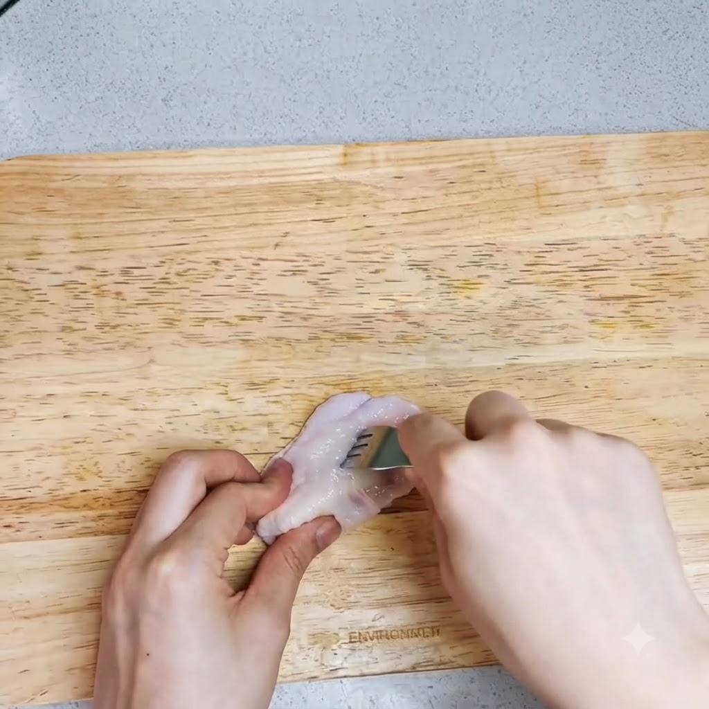 まな板の上の生の手羽先にフォークで穴を開けている手。