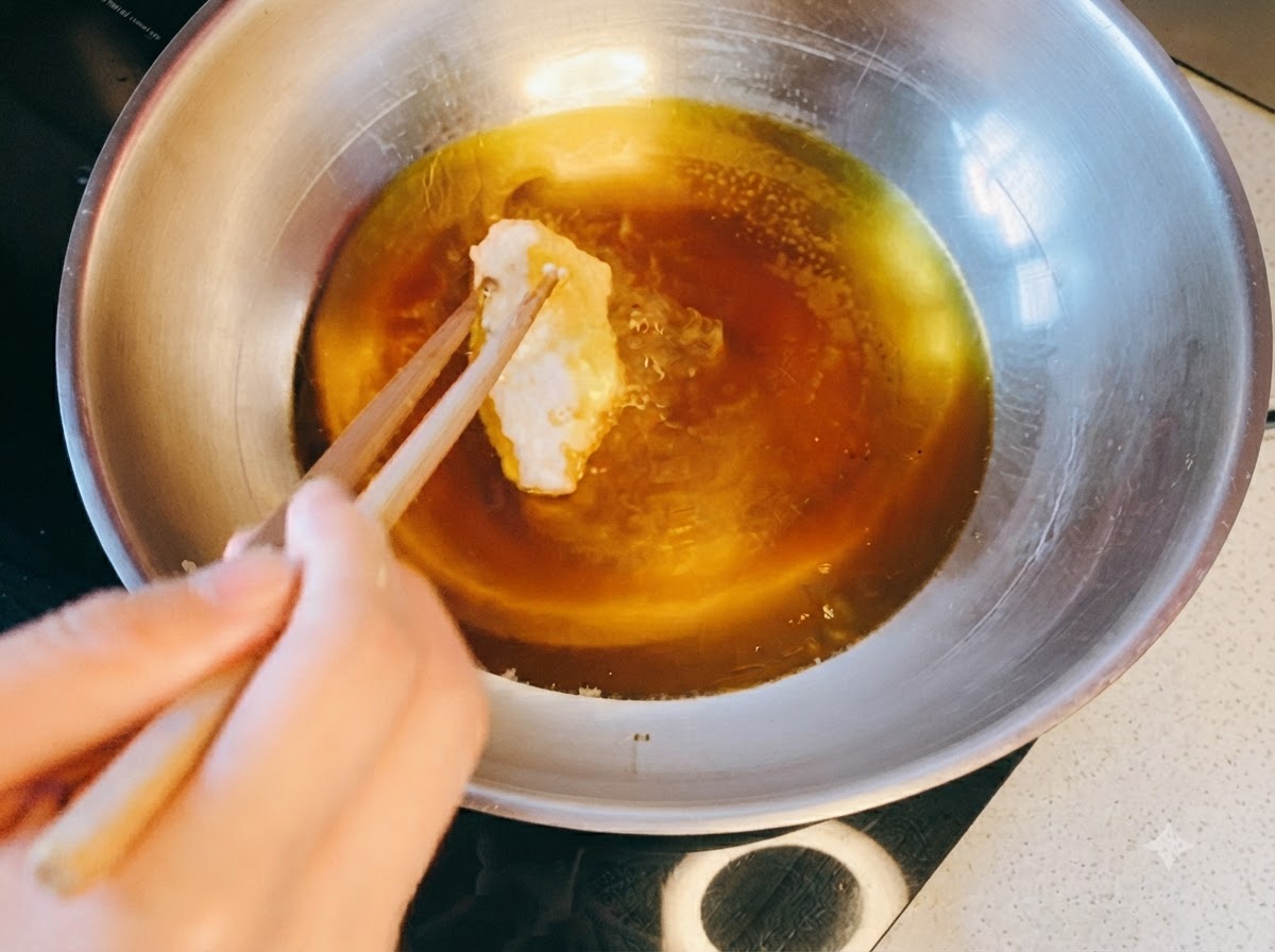 箸を使って、油を熱した金属製のフライパンに衣をつけた鶏肉を入れている様子。