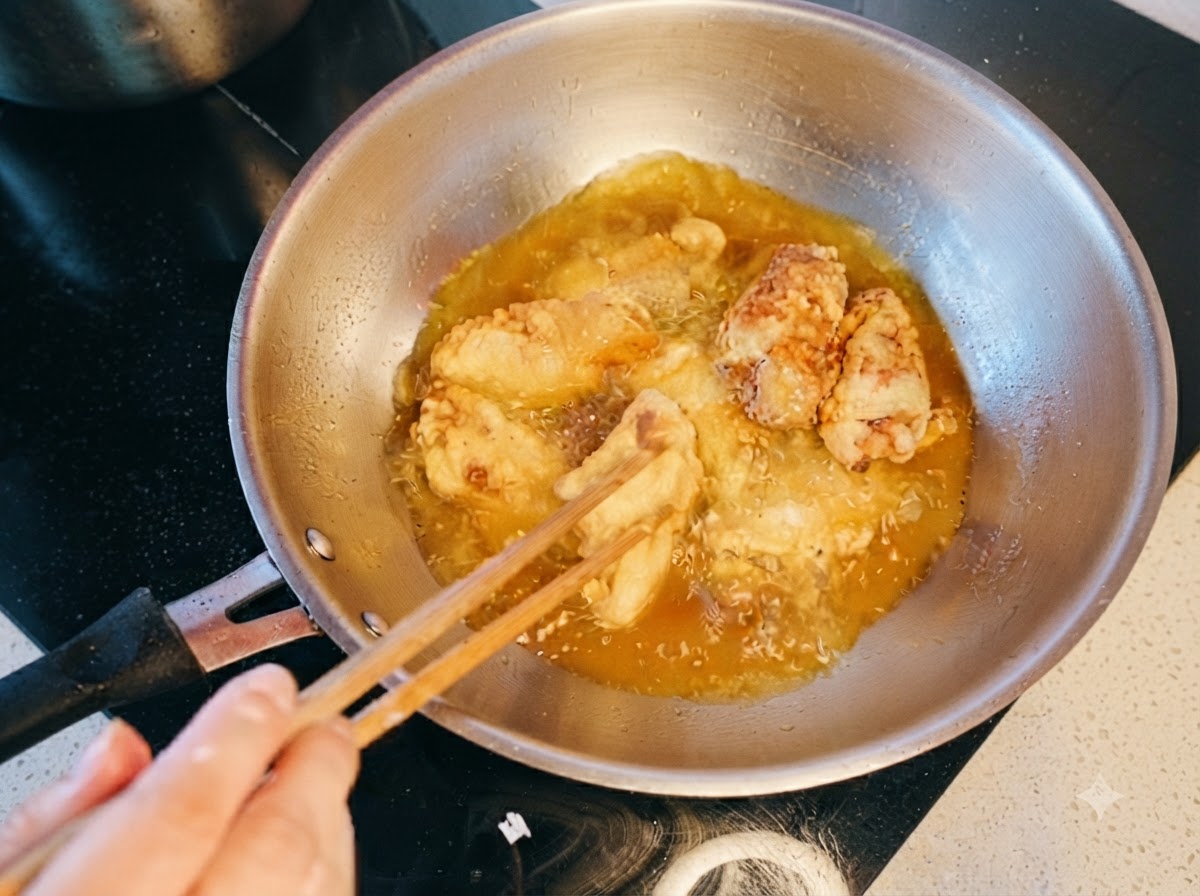 箸を使って熱い油の中で鶏肉をかき混ぜながら二度揚げしている様子。