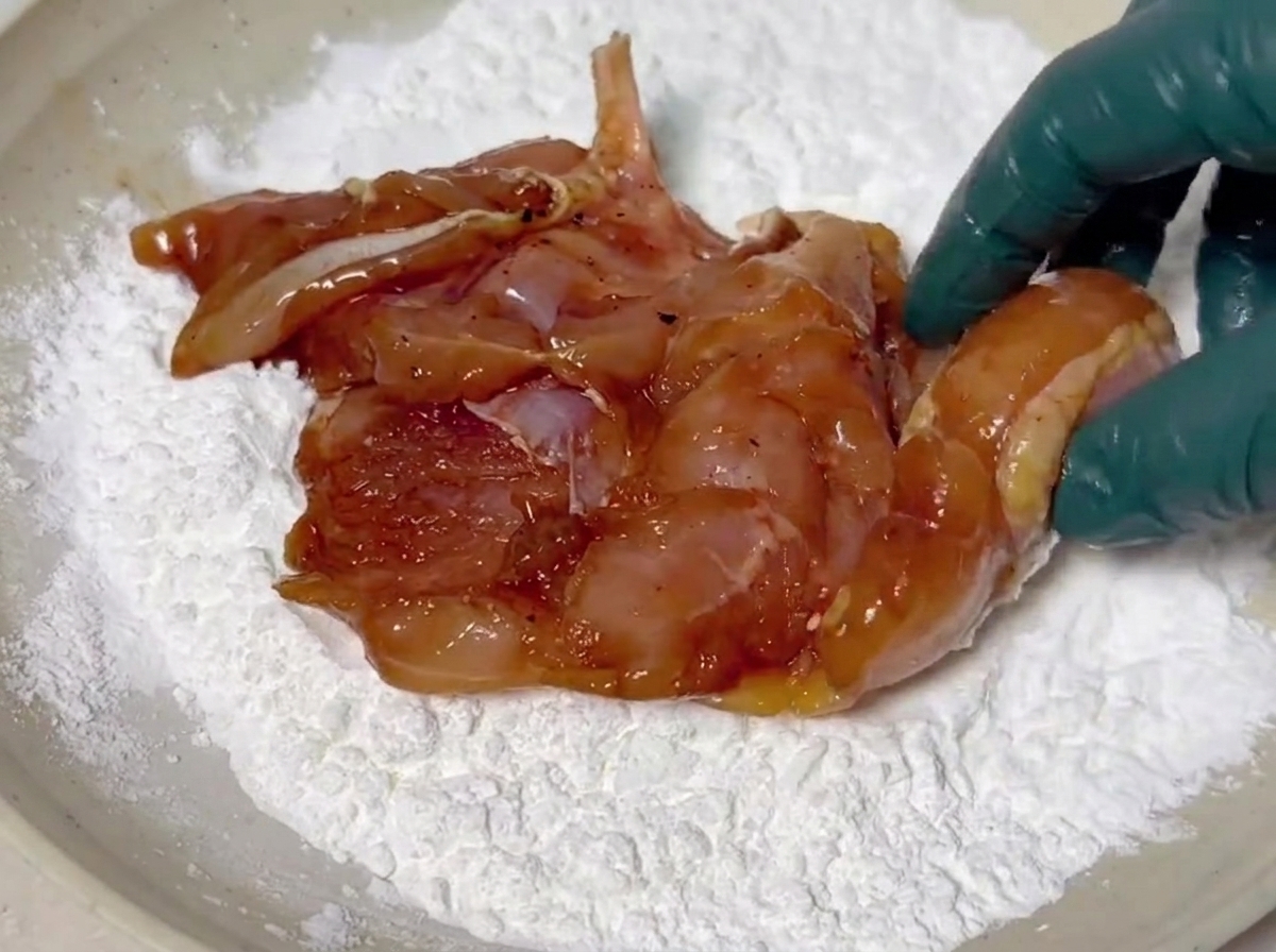 下味のついた鶏肉に、浅いお皿で片栗粉の白い衣をまぶしている様子。